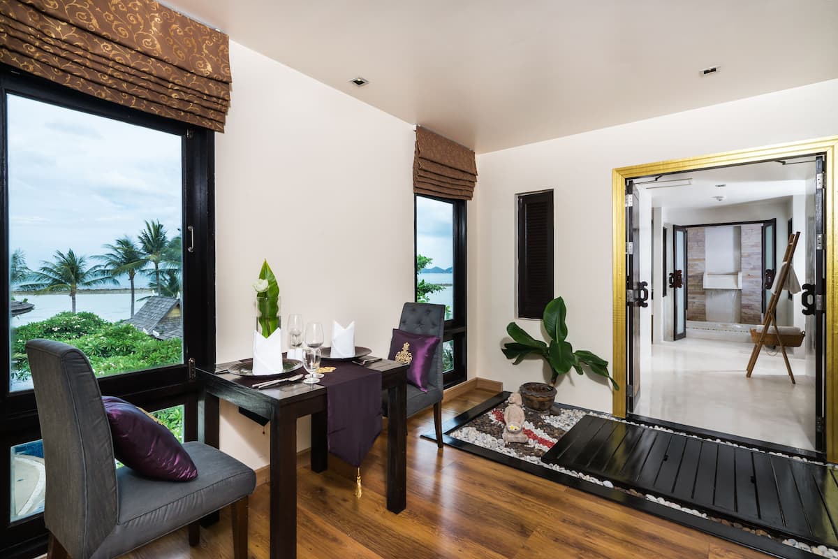 A dining area with a view of palm trees, a table set for two, and a large window with curtains.