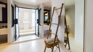 Un baño moderno con un espejo grande, una escalera de madera y un sillón de mimbre.