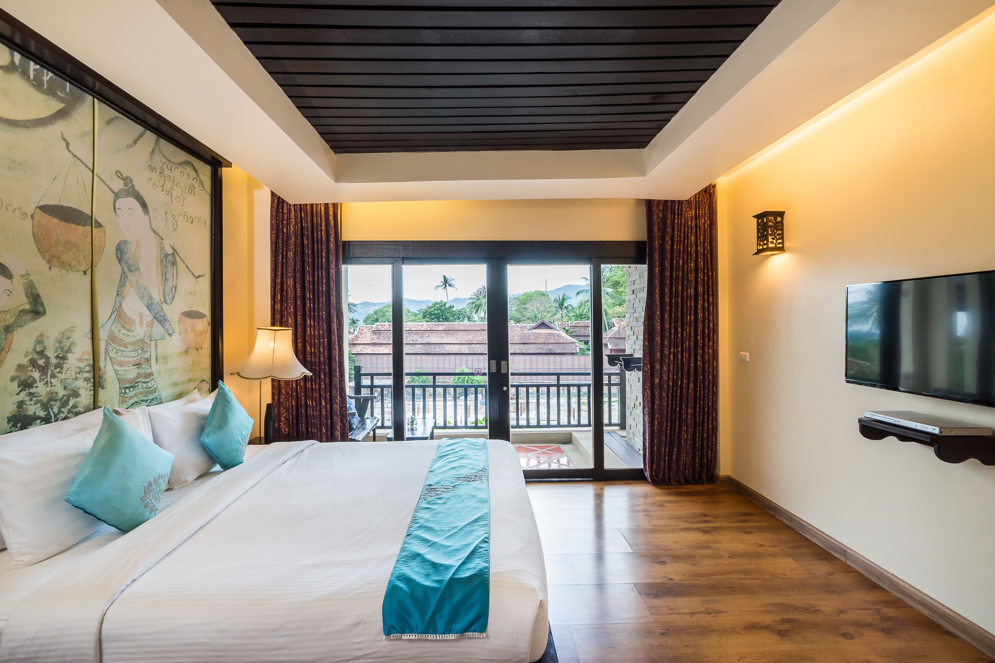 A hotel room with a large bed, a TV mounted on the wall, and a balcony with a view of the surroundings.
