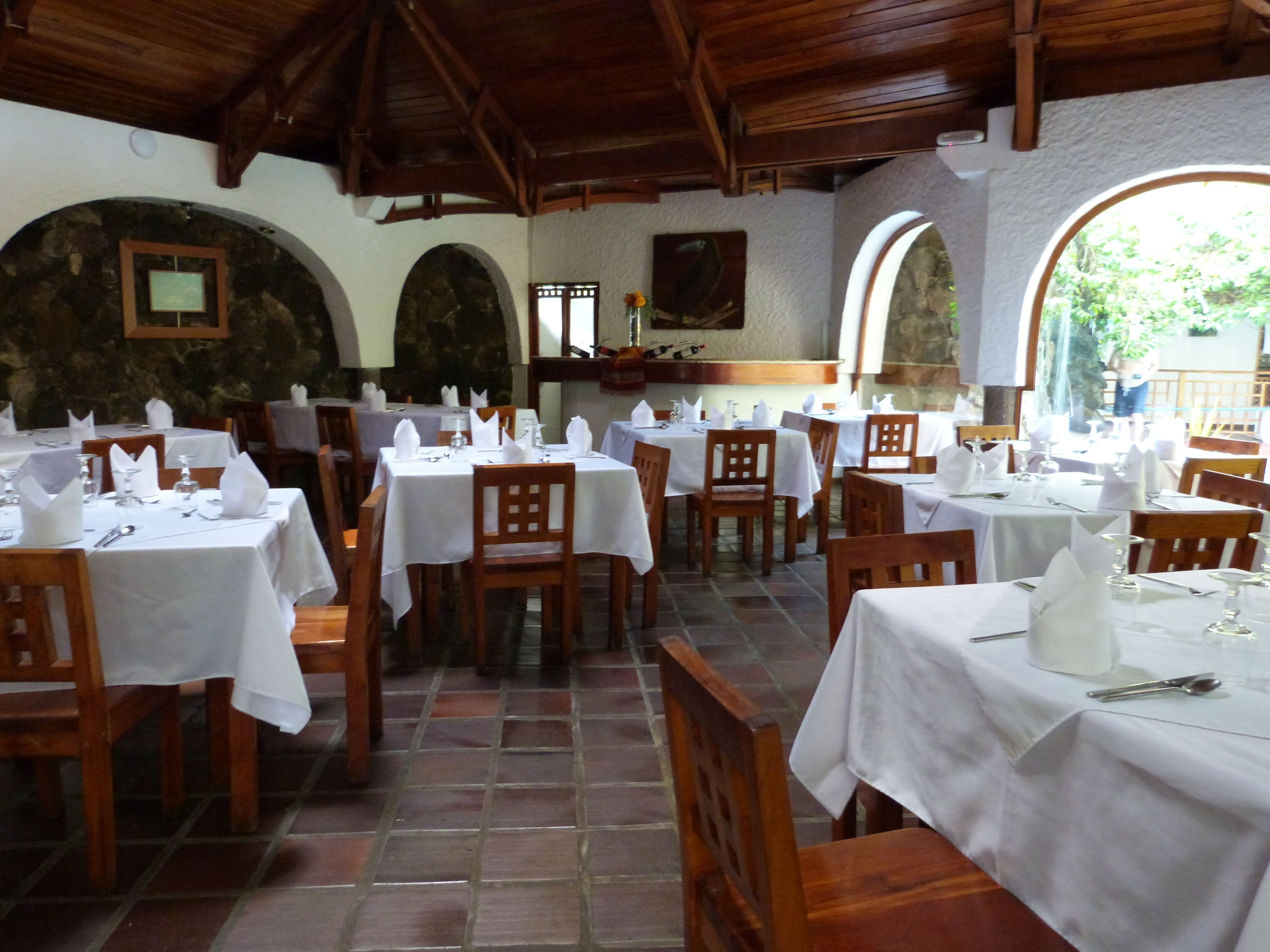 Un restaurante con varias mesas dispuestas para comer, sillas de madera y una pared de piedra.