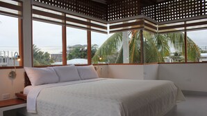 A bedroom with a large bed, a wooden slatted ceiling, and a view of palm trees and buildings outside. - Hotel Silberstein (Puerto Ayora)