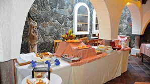 A breakfast buffet with a stone wall backdrop and arched windows. - Hotel Silberstein (Puerto Ayora)