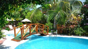 A swimming pool with a wooden bridge, surrounded by lush greenery and palm trees. - Hotel Silberstein (Puerto Ayora)