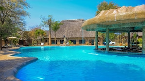 A swimming pool with lounge chairs and umbrellas, a bar area, and a thatched-roof building. - Chrismar Hotel Livingstone (Livingstone)