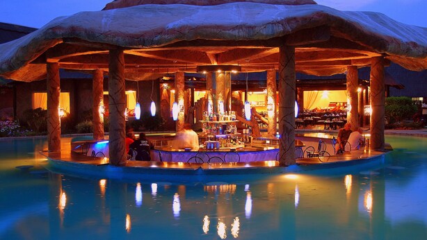 A bar area with a unique rock-like structure overhead, surrounded by a pool. - Chrismar Hotel Livingstone (Livingstone)