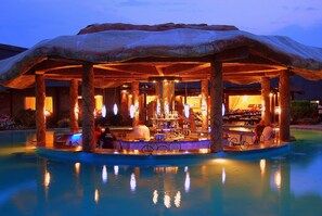 A bar area with a unique rock-like structure overhead, surrounded by a pool. - Chrismar Hotel Livingstone (Livingstone)
