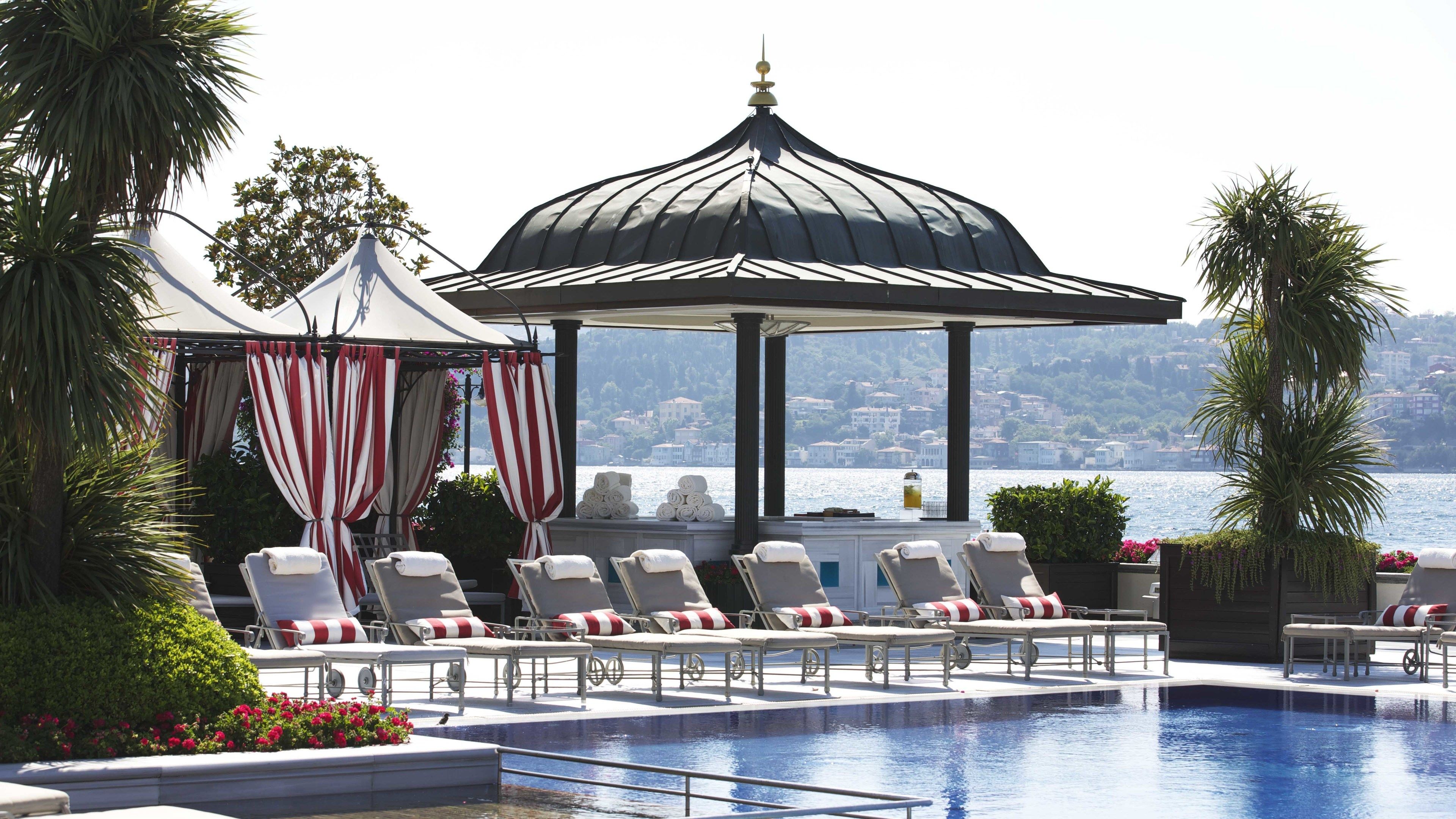 Área à beira da piscina com espreguiçadeiras, um gazebo e vista para um corpo d'água.