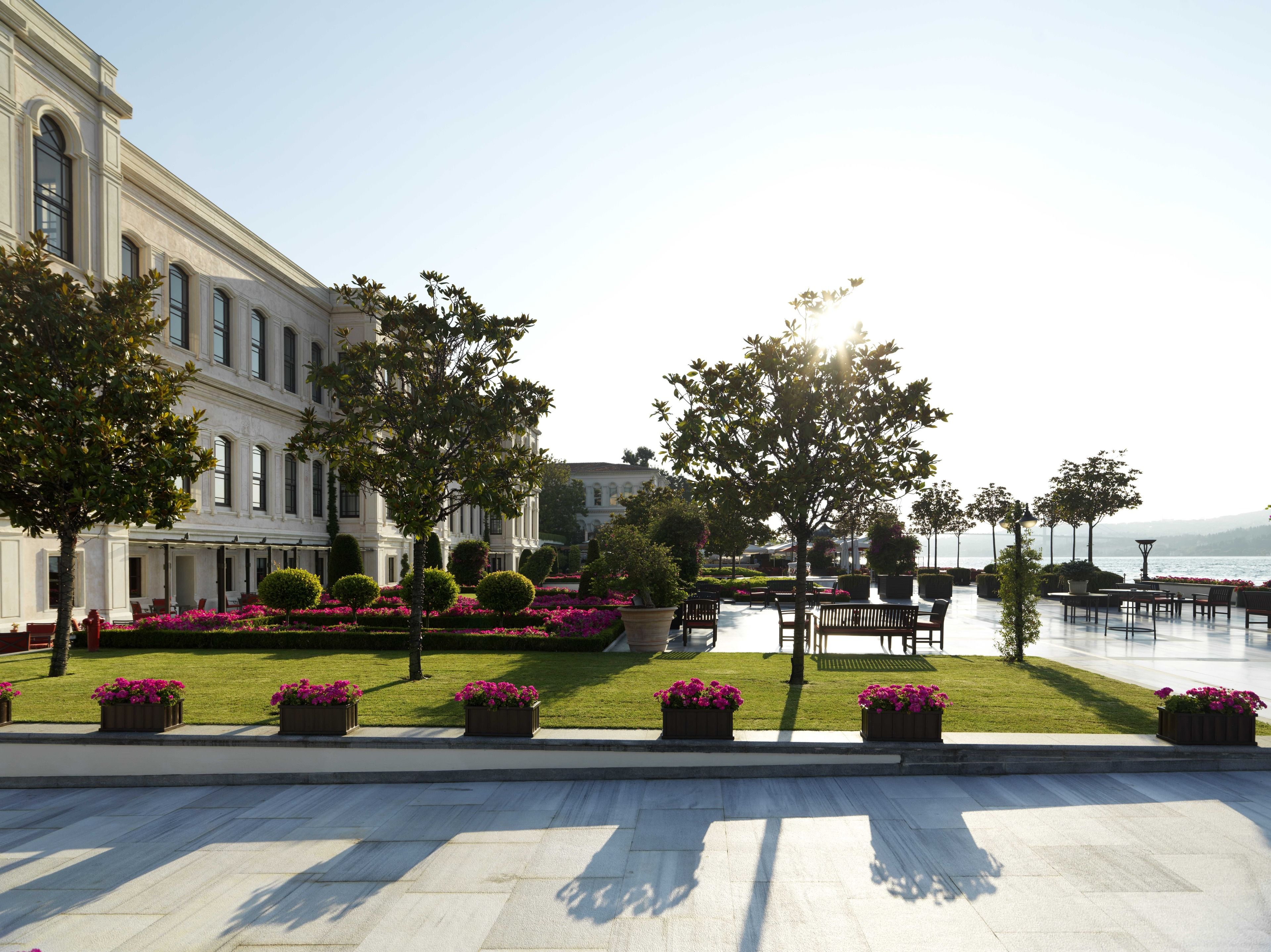 A courtyard with a large building, seating areas, and a view of the sea.