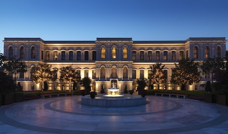 A large, classical building with a central fountain, surrounded by a circular courtyard with benches and trees.