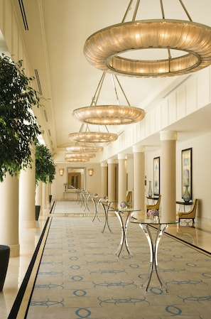 A spacious hotel lobby with a long corridor, elegant chandeliers, and modern furniture.