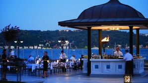An outdoor dining area with tables and chairs, a bar, and a gazebo with a fire feature. - Four Seasons Hotel Istanbul at the Bosphorus (Istanbul)