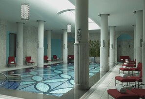 A spacious indoor pool area with red lounge chairs, large white columns, and a patterned floor.
