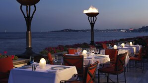 An outdoor dining area with tables set for two, overlooking a body of water. - Four Seasons Hotel Istanbul at the Bosphorus (Istanbul)