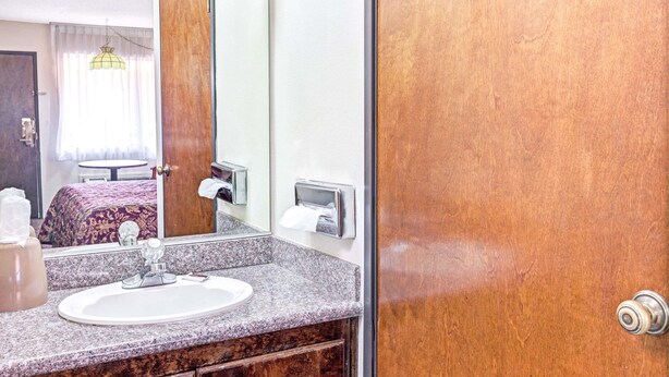 A hotel bathroom with a granite countertop sink, a mirror, a towel dispenser, and a wooden door. - Vantage Point Inn Woodland Hills (Woodland Hills)