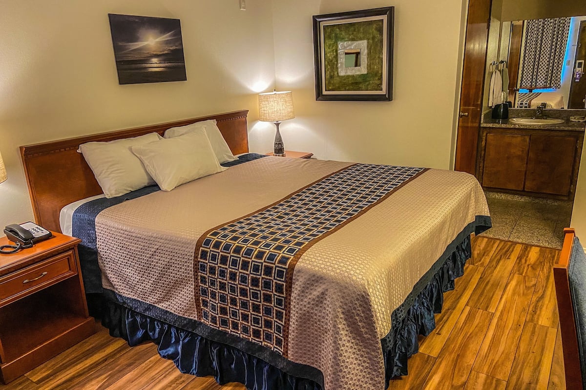A neatly made bed with a patterned bedspread, a bedside lamp, and a nightstand with a phone.