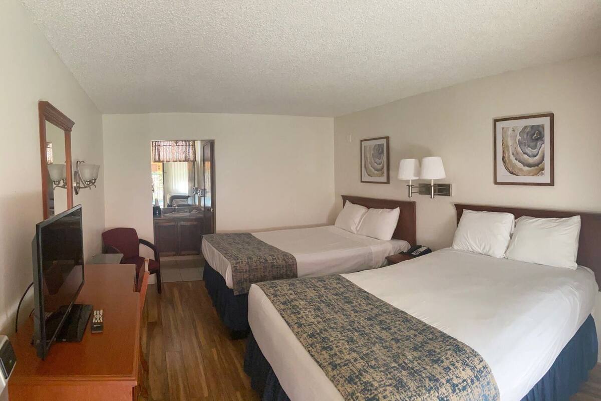 A hotel room with two beds, a desk, a chair, a television, and artwork on the walls.