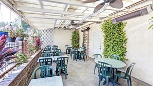 Une terrasse extérieure avec des tables et des chaises, un ventilateur de plafond et des plantes en pot.