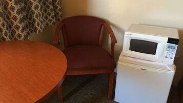 A compact kitchenette with a microwave on a Haier refrigerator, a wooden dining table, and a patterned curtain.