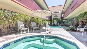 Un espace piscine aménagé avec des chaises longues et des parasols, entouré de verdure et doté d’un bord de piscine carrelé.