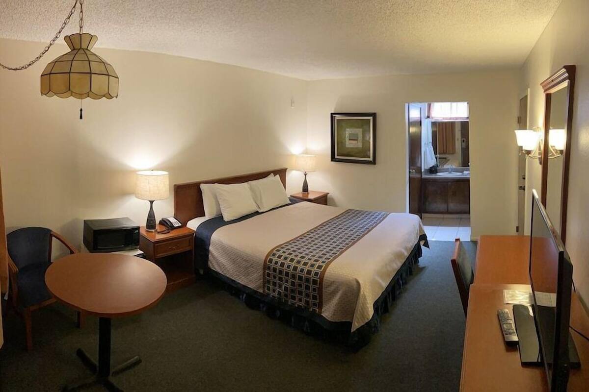 A hotel room with a bed, bedside lamps, a desk, a chair, a television, and a mirror.