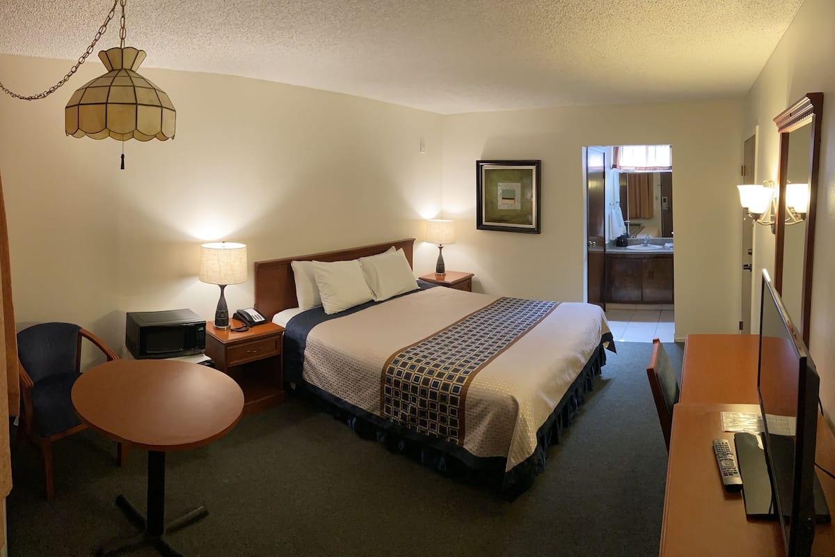 A hotel room with a bed, bedside lamps, a desk with a telephone, a chair, a television, and a mirror.
