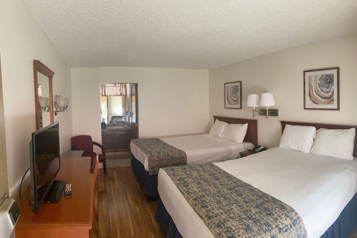 A hotel room with two beds, a desk, a chair, a TV, and artwork on the walls.
