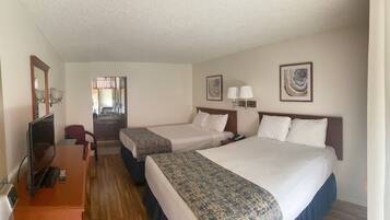A hotel room with two beds, a desk, a chair, a TV, and artwork on the walls.