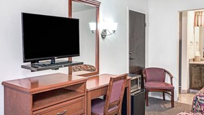 Une chambre d’hôtel équipée d’un bureau en bois, d’un téléviseur à écran plat, d’une chaise, d’un four à micro-ondes et d’une porte donnant accès à une salle de bain.