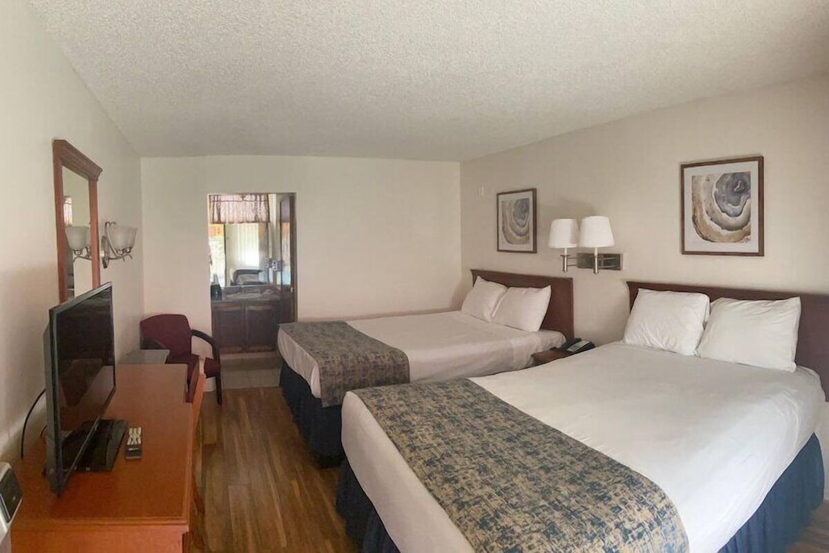 A hotel room with two beds, a desk, a chair, a television, and artwork on the walls.