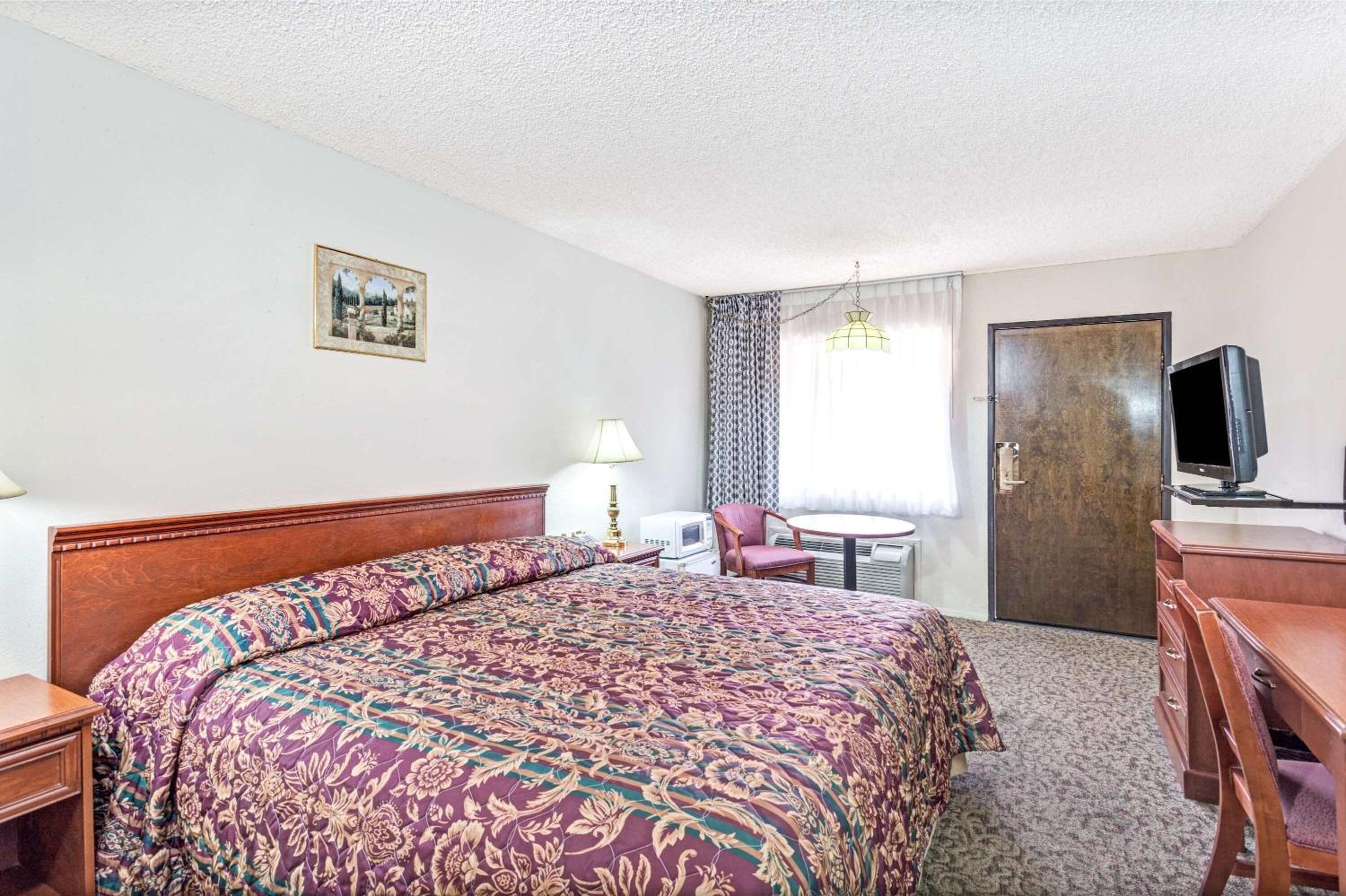A hotel room with a large bed, a desk, a chair, a television, and a door.