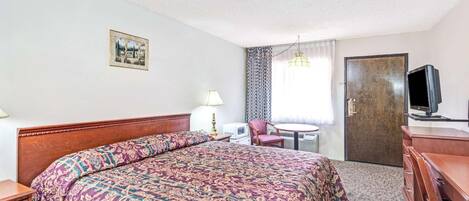 A hotel room with a large bed, a desk, a chair, a television, and a door.