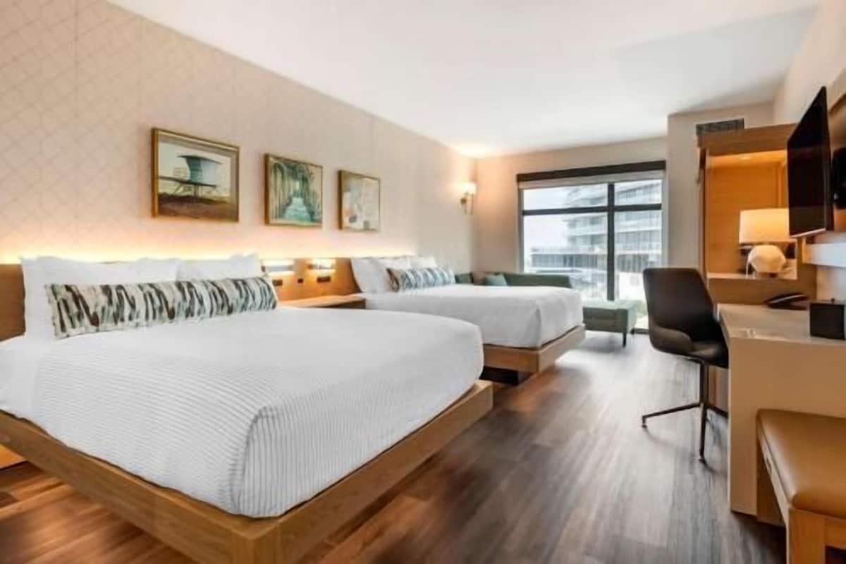 Una camera d'albergo con due letti, una scrivania e una sedia.