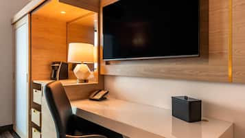 Een moderne hotelkamer met een houten bureau, een flatscreen televisie aan de wand, een lamp, een telefoon en een klein zwart kastje op het bureau.