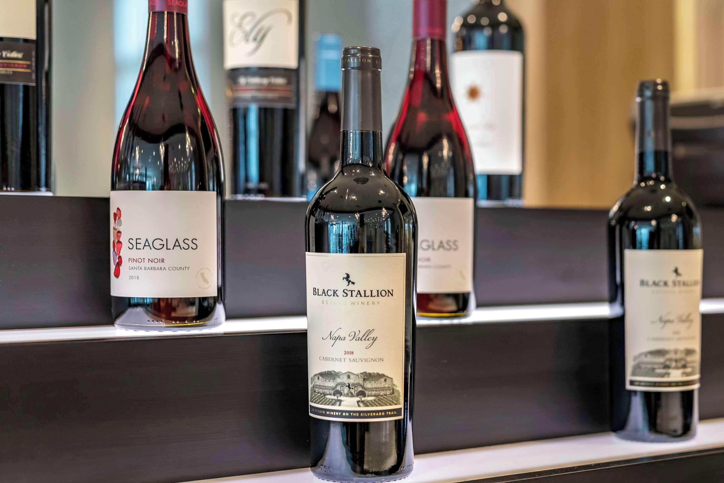 A selection of wine bottles on a shelf, including Seaglass Pinot Noir and Black Stallion Napa Valley Cabernet Sauvignon.