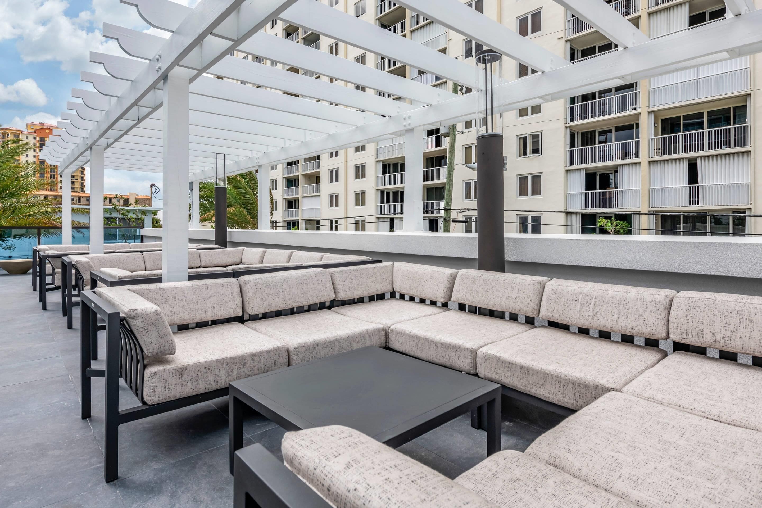 A rooftop lounge area with outdoor seating and a pool in the background.