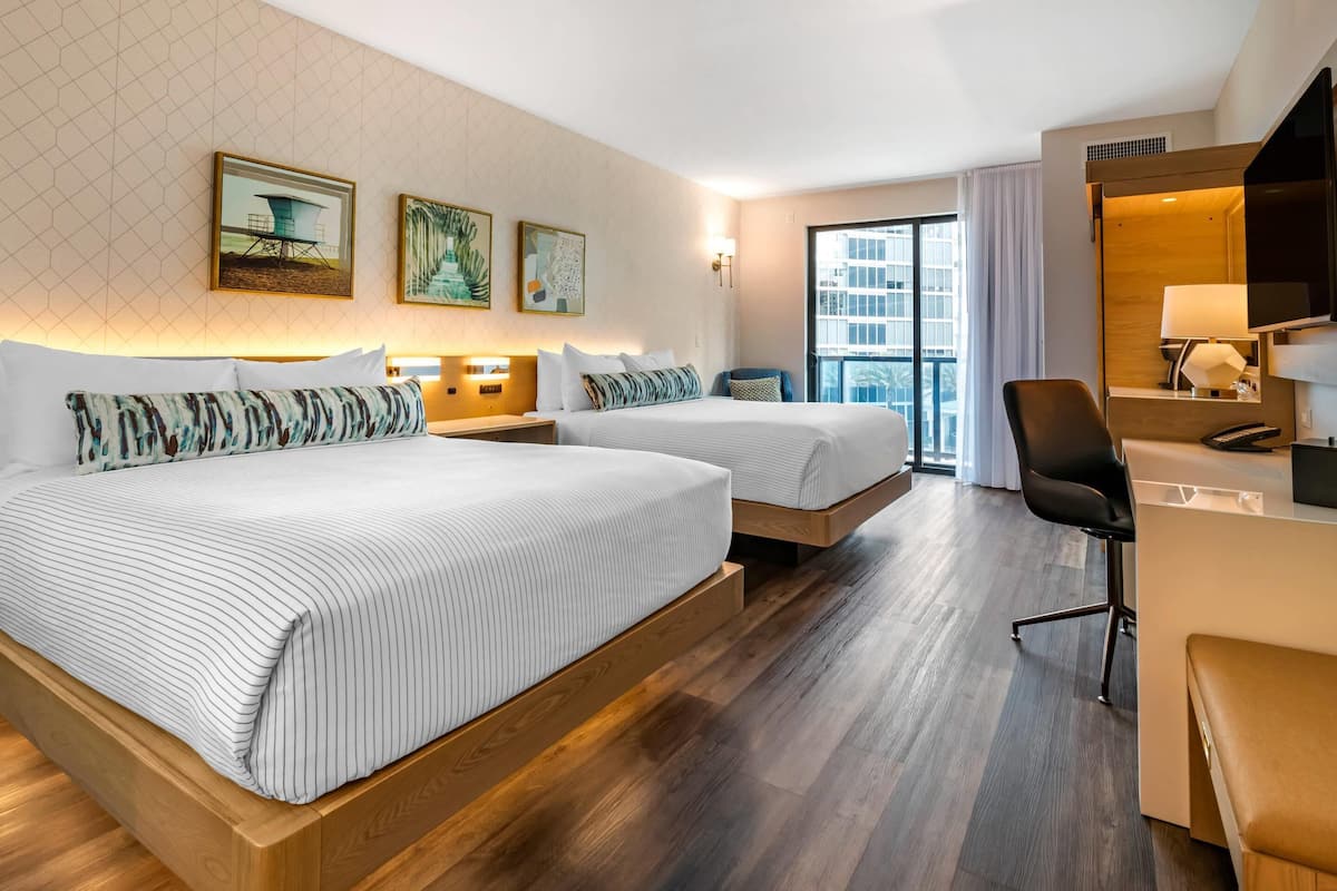 Habitación de hotel con dos camas, un escritorio, una silla y un amplio ventanal.
