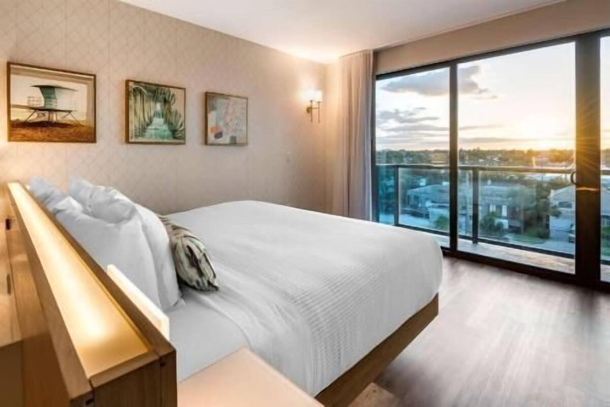 Una camera d'hotel con un letto grande, un comodino e una vista sulla città attraverso ampie finestre.