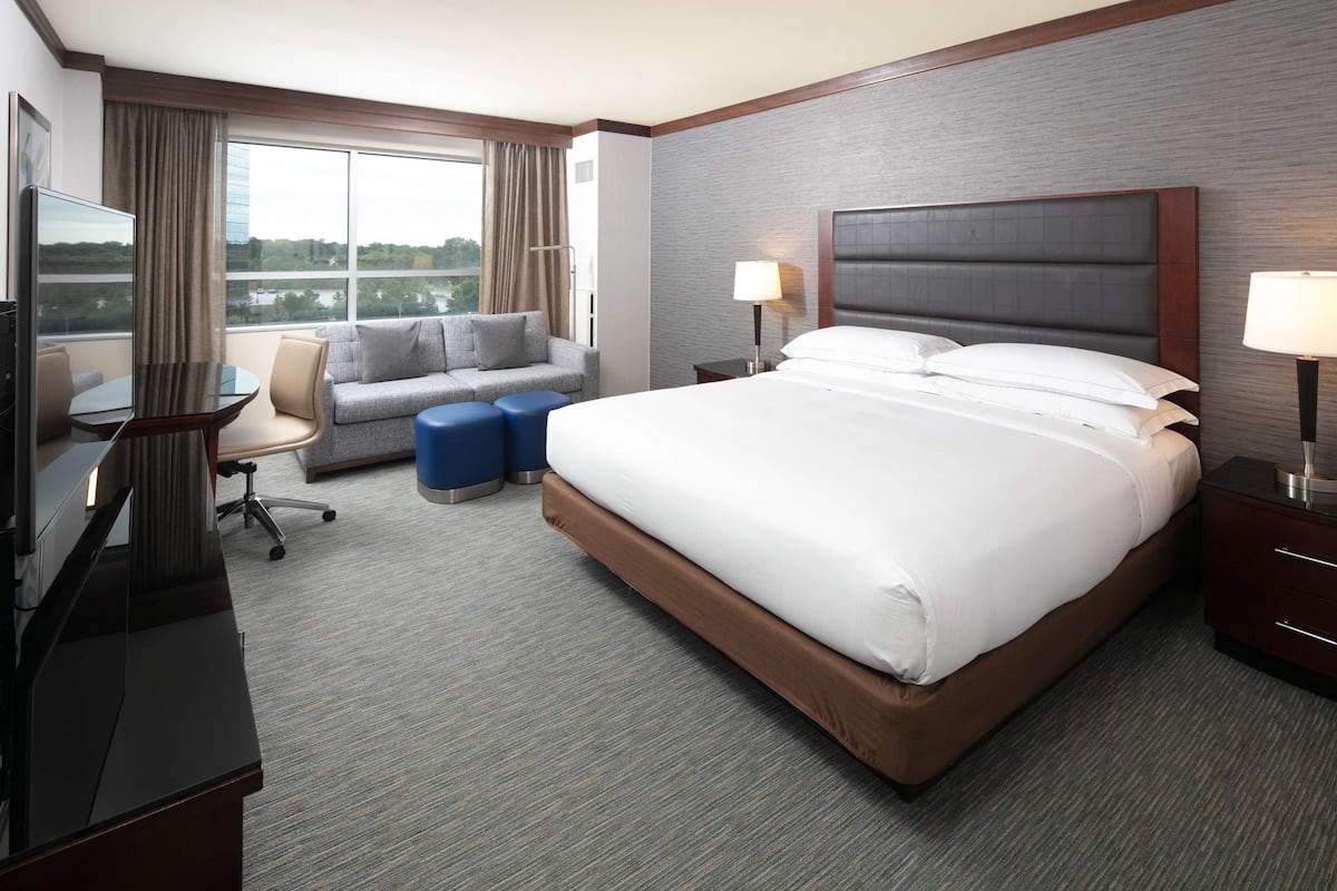 A hotel room with a large bed, a desk with a computer, a sofa, and a TV.