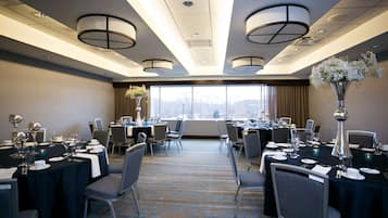 Un salón de conferencias con varias mesas dispuestas para comidas, ventanas amplias y vistas a las montañas.
