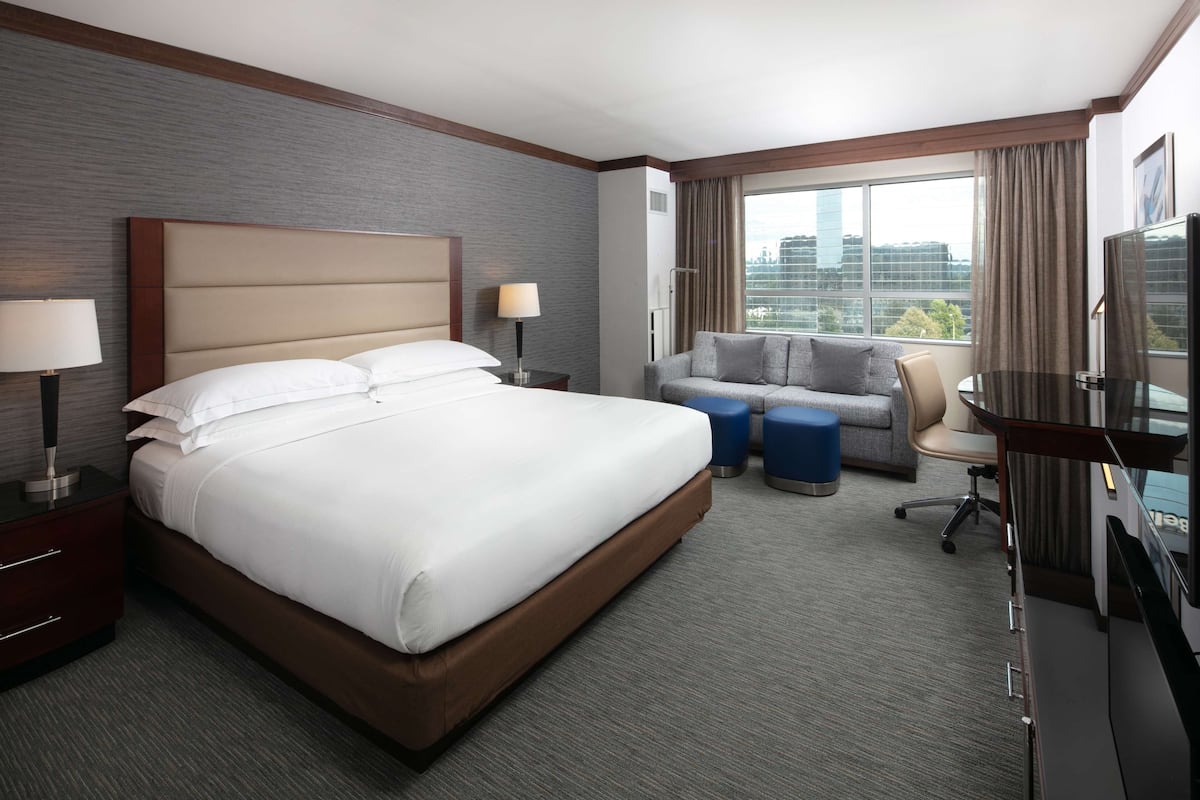 A hotel room with a large bed, a sofa, a TV, and a window with a city view.