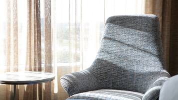 Una habitación con un sillón estampado, una mesita redonda pequeña y cortinas traslúcidas.
