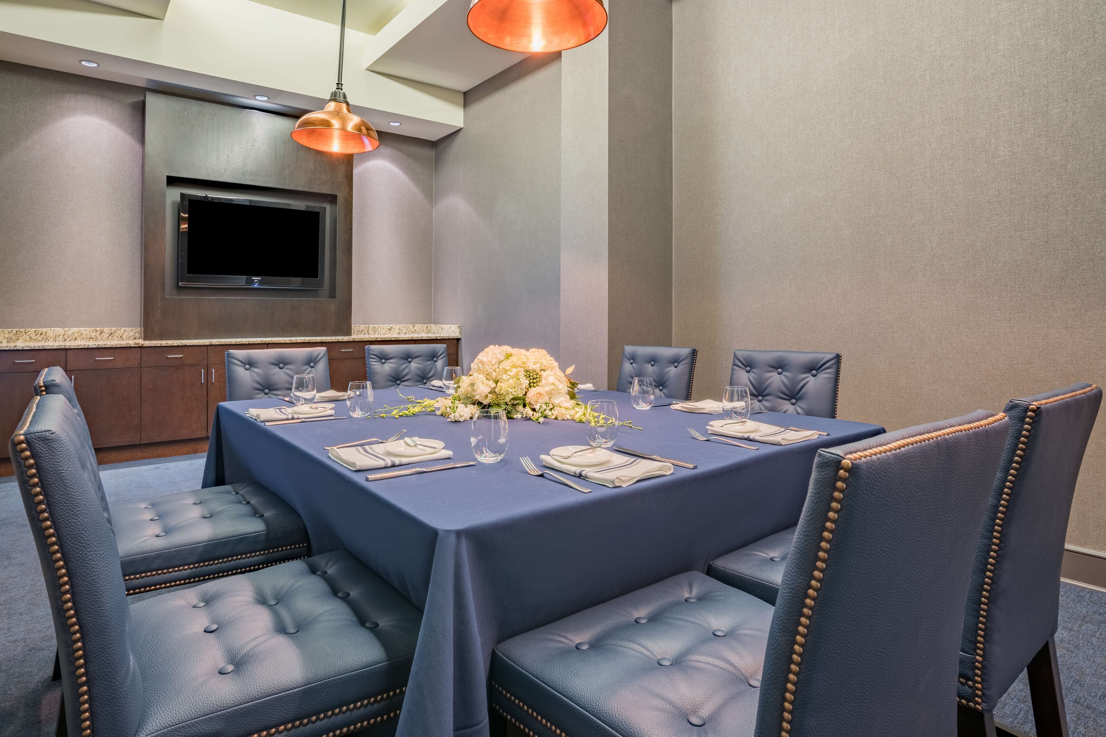 A dining area with a rectangular table set for six, surrounded by upholstered chairs with tufted backs.