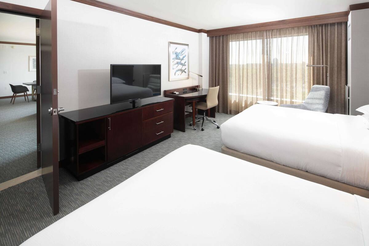 A hotel room with a large bed, a desk with a chair, a television, and a window with curtains.