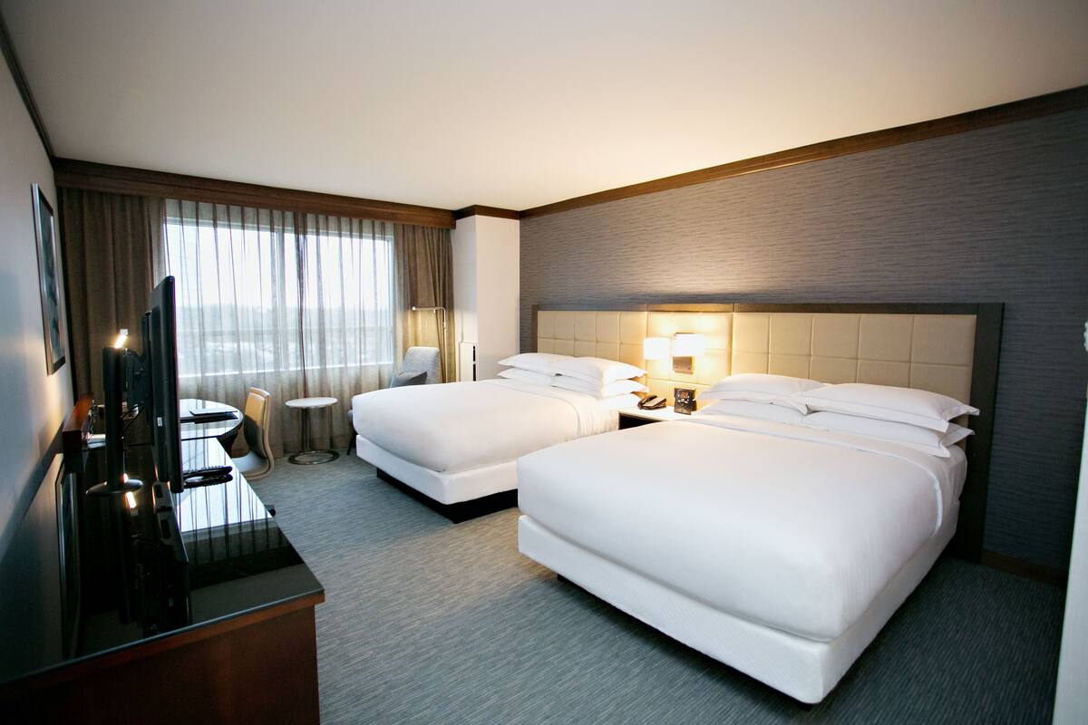 A hotel room with two beds, a desk with a TV, and a small round table.