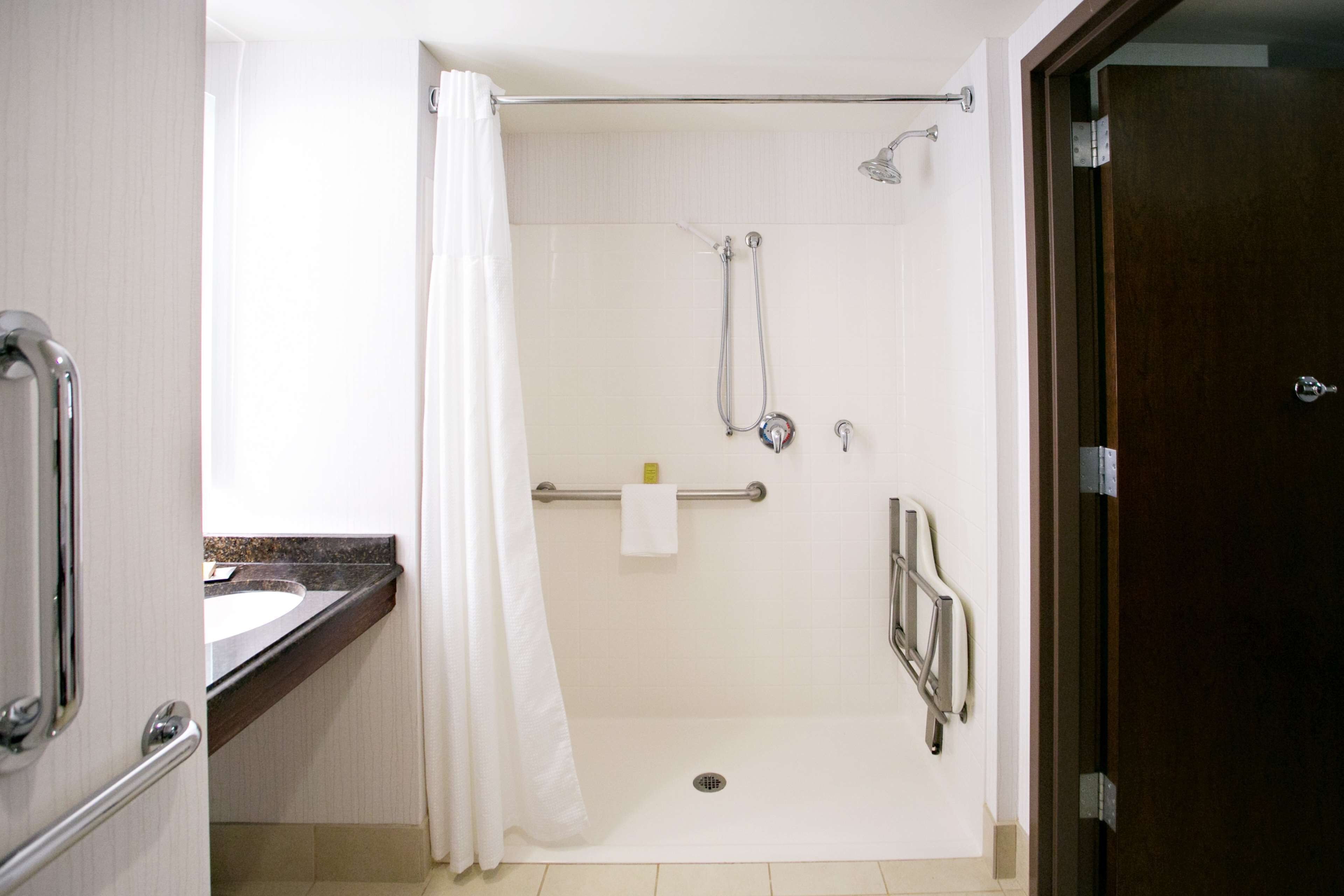 Une douche à l’italienne avec une porte en verre, une barre d’appui, un porte-serviettes et un pommeau de douche.