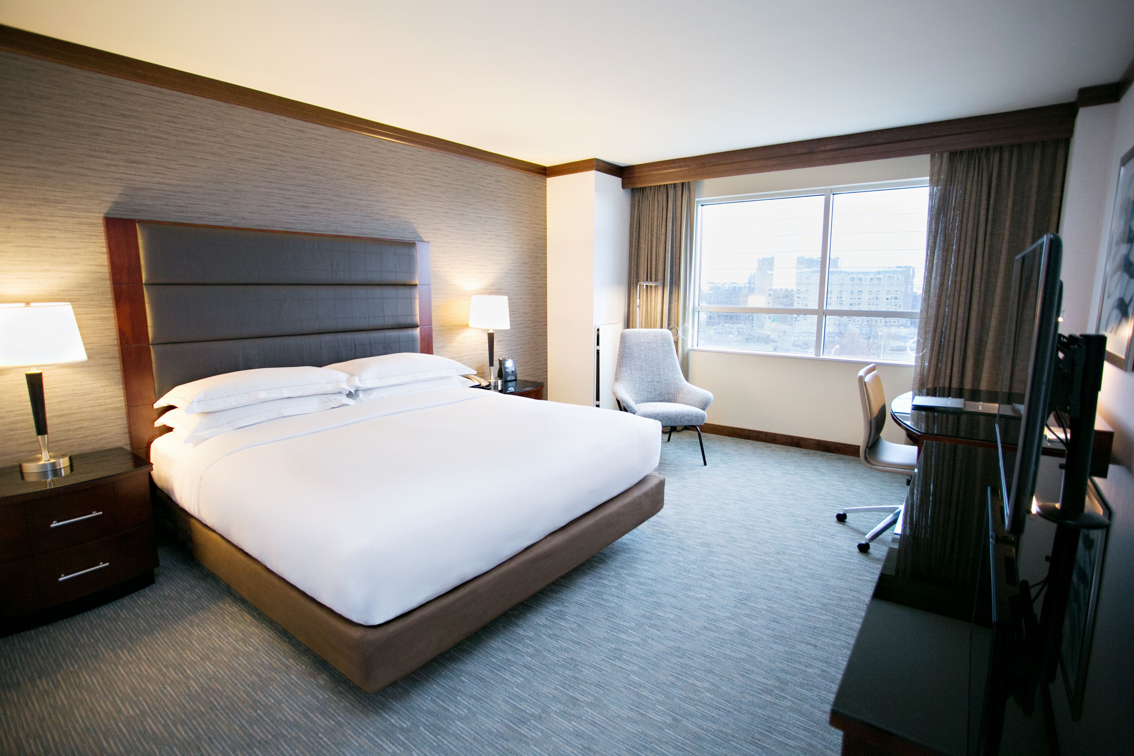 A hotel room with a large bed, a desk with a chair, a TV, and a window with curtains.