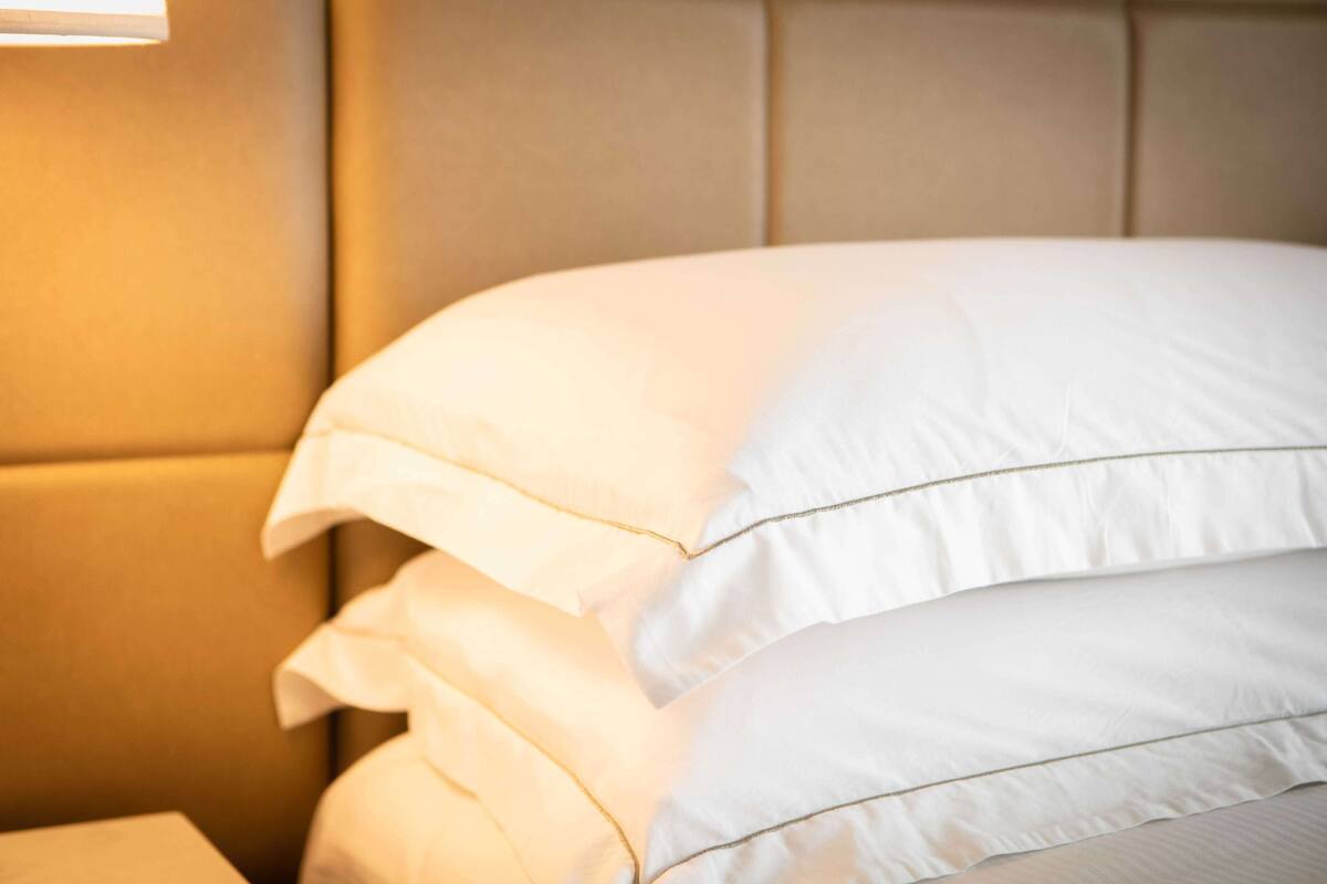 A neatly made bed with white linens and a headboard.