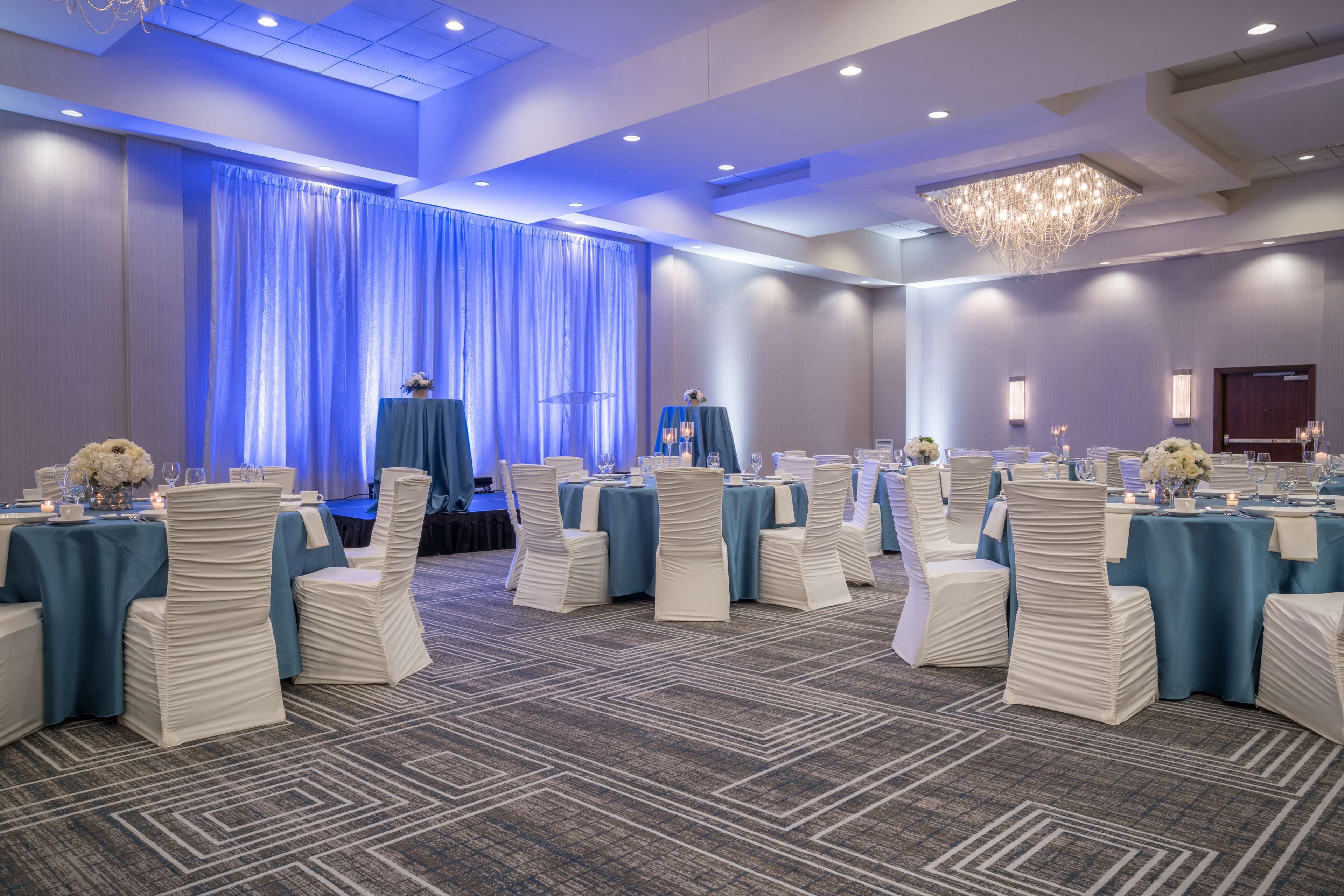 A banquet hall with round tables, white chairs, and blue tablecloths.