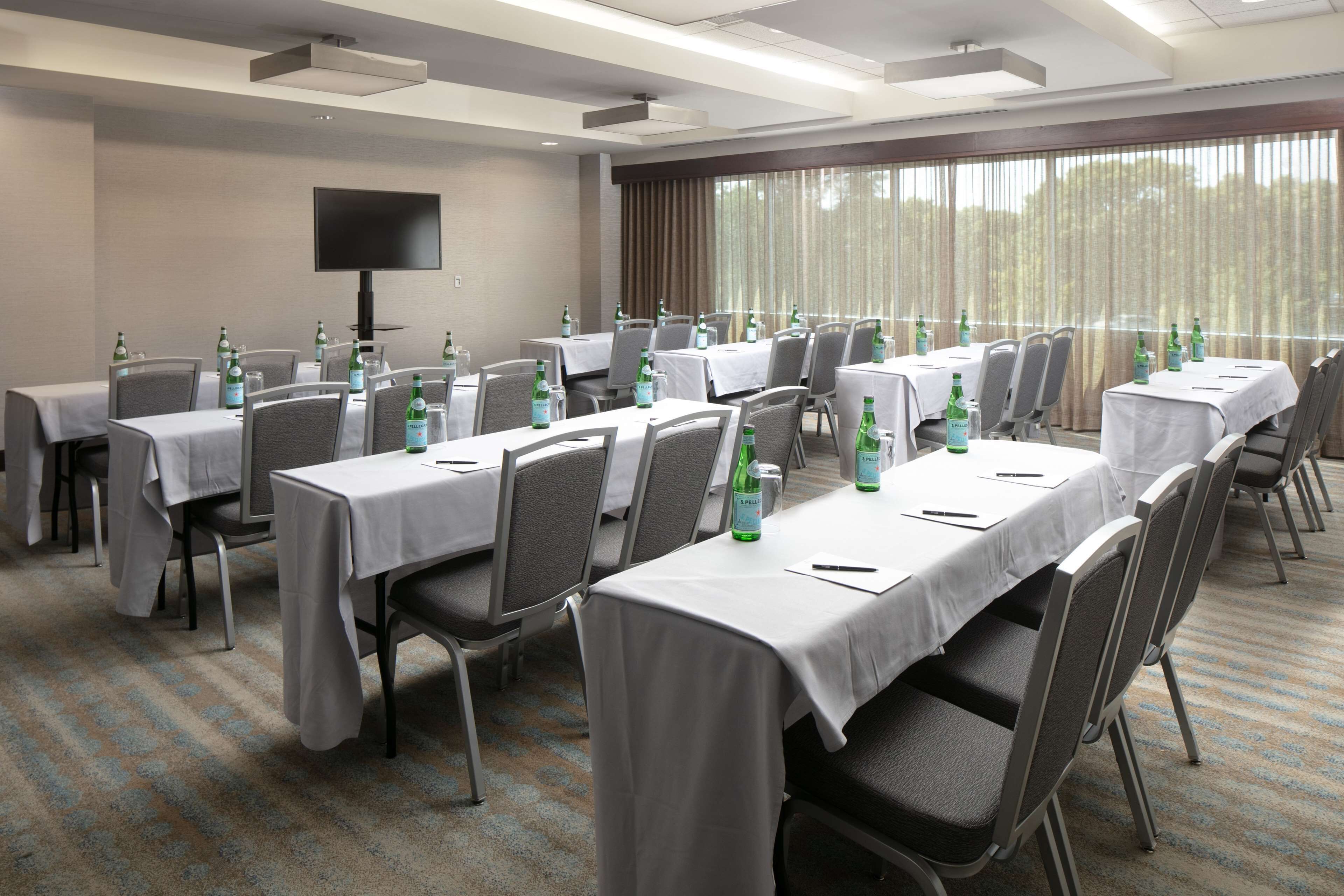 A conference room with tables set for meetings, equipped with chairs and tables, and a large screen on the wall.