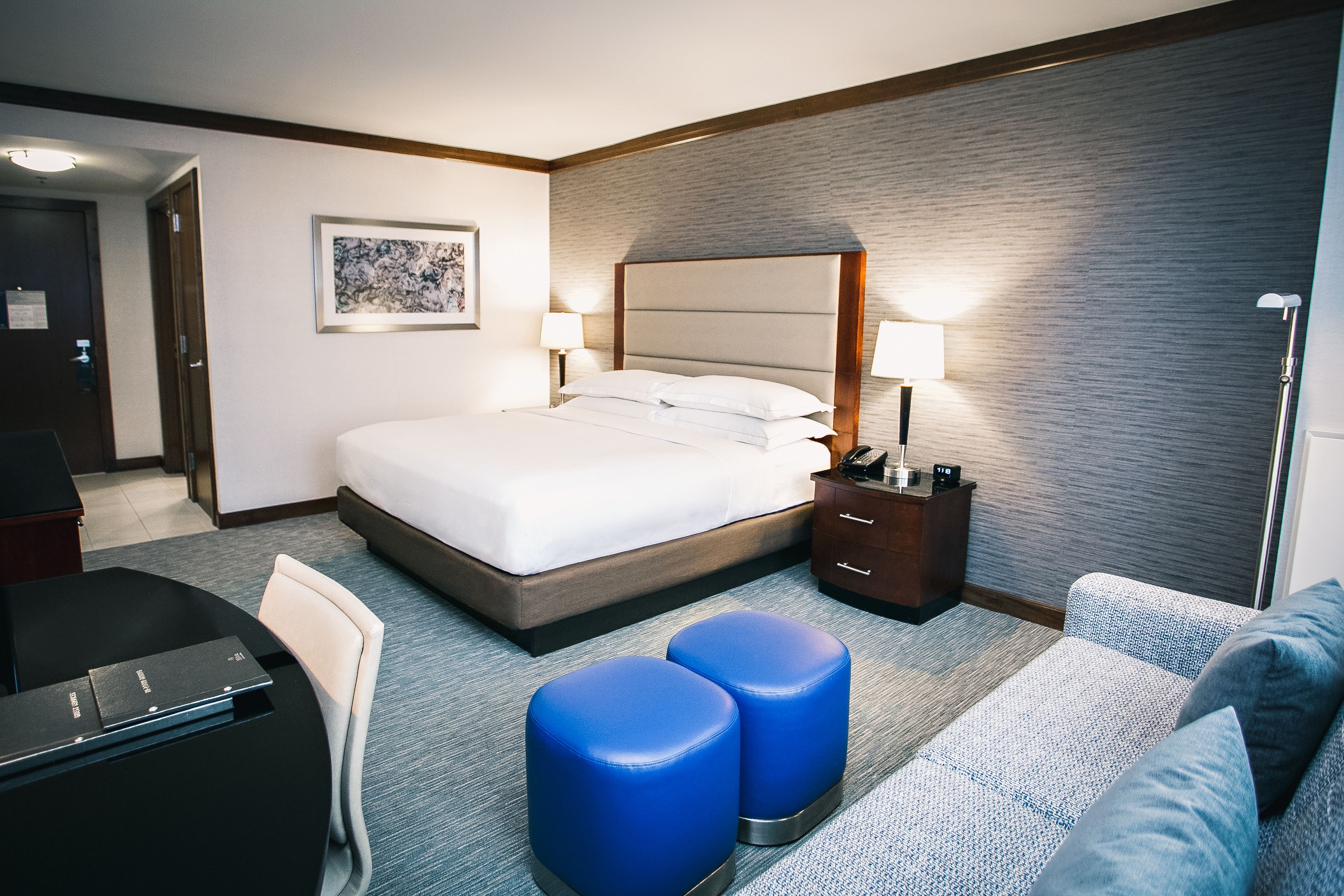A hotel room with a bed, bedside tables, a desk, and a sofa.